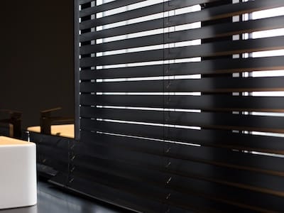 Wood blinds Coulisse black color closeup on the window. Wooden plate 50mm wide. Venetian blinds in the bathroom. Black tap, mirror near the washbasin.