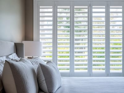A set of luxury white plantation shutters installed indoors in a bedroom, captured with a selective focus for a refined aesthetic